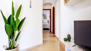 Een gang met een grote plant, een flatscreen televisie en een kleine cactus op een plank.