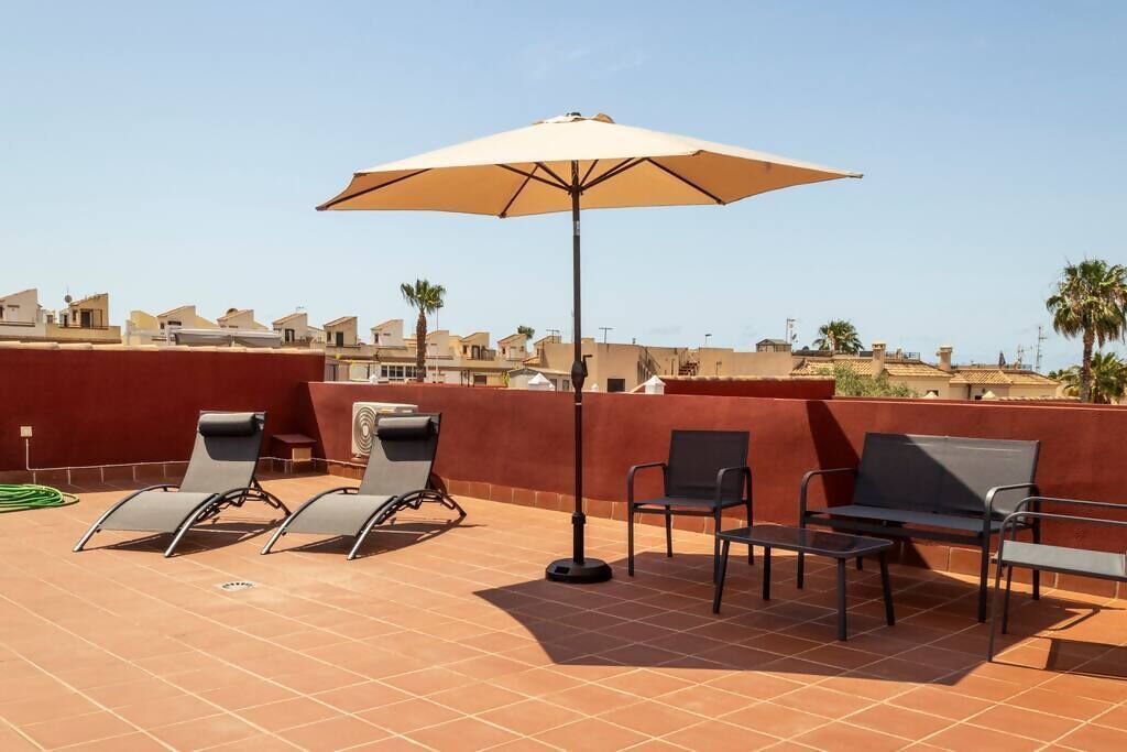 A rooftop terrace with four lounge chairs, a table, and a large umbrella.