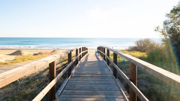 Een houten looppad dat naar een strand leidt, met een helder uitzicht op de oceaan.