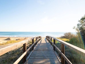 A wooden boardwalk leading to a beach with a clear view of the ocean.