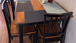 A dining area with a wooden table and chairs, a vase of sunflowers, and a kitchen in the background.