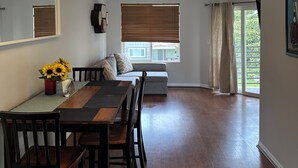 A dining area with a wooden table and chairs, a sofa, and a window with blinds.