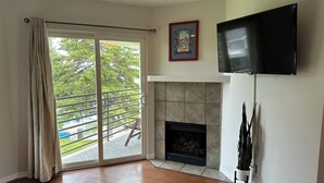 A living room with a fireplace, a TV mounted on the wall, and a sliding glass door leading to a balcony.