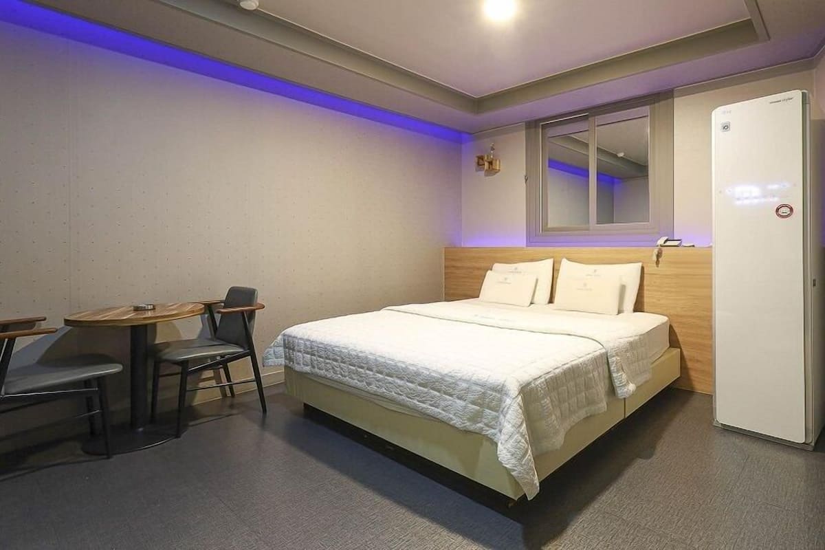 A hotel room with a bed, a desk, and a chair, a mirror, and a door.