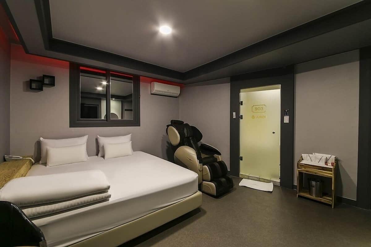 A modern hotel room with a large bed, a massage chair, an air conditioning unit, and a small table with a tray.