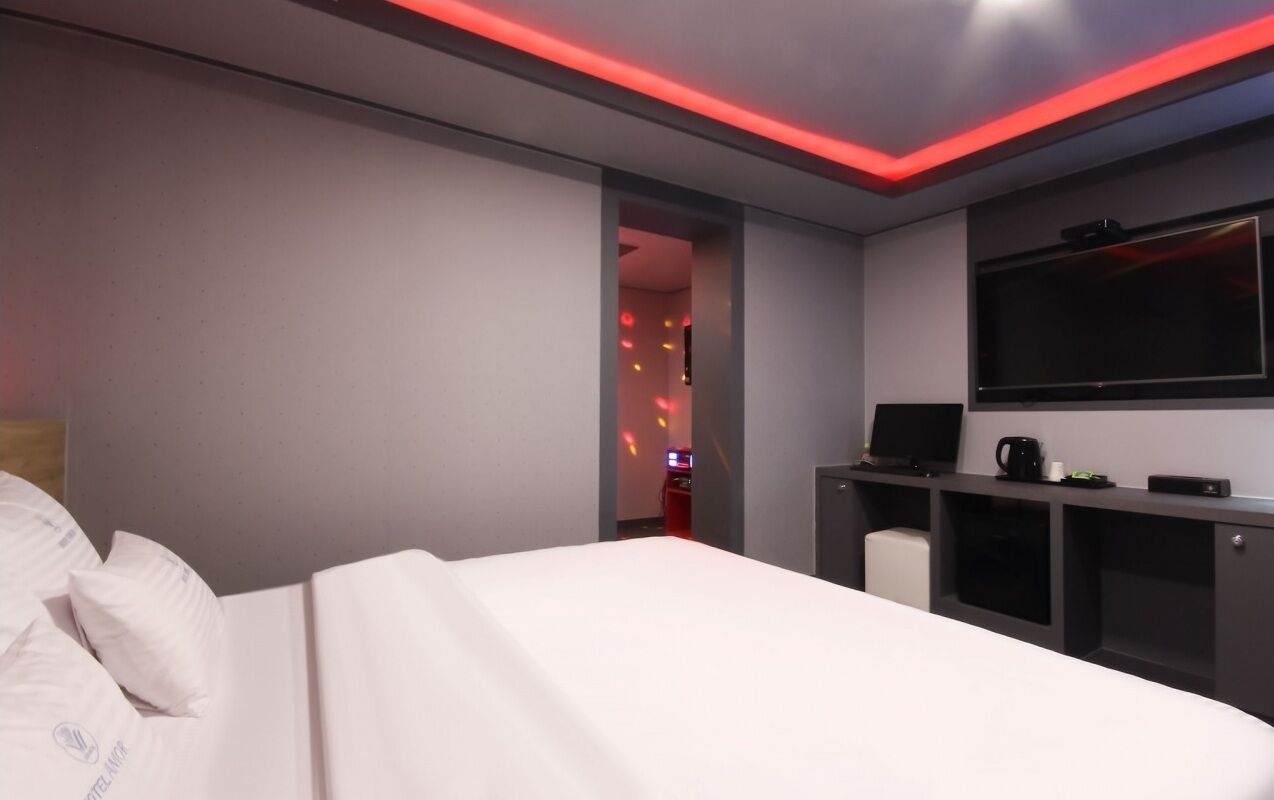 A modern hotel room with a bed, a desk with a flat-screen TV, and a coffee machine.