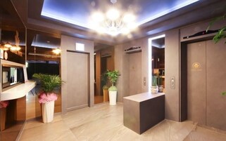 A modern hotel lobby with a reception desk, a chandelier, and a reception area with a counter and potted plants.