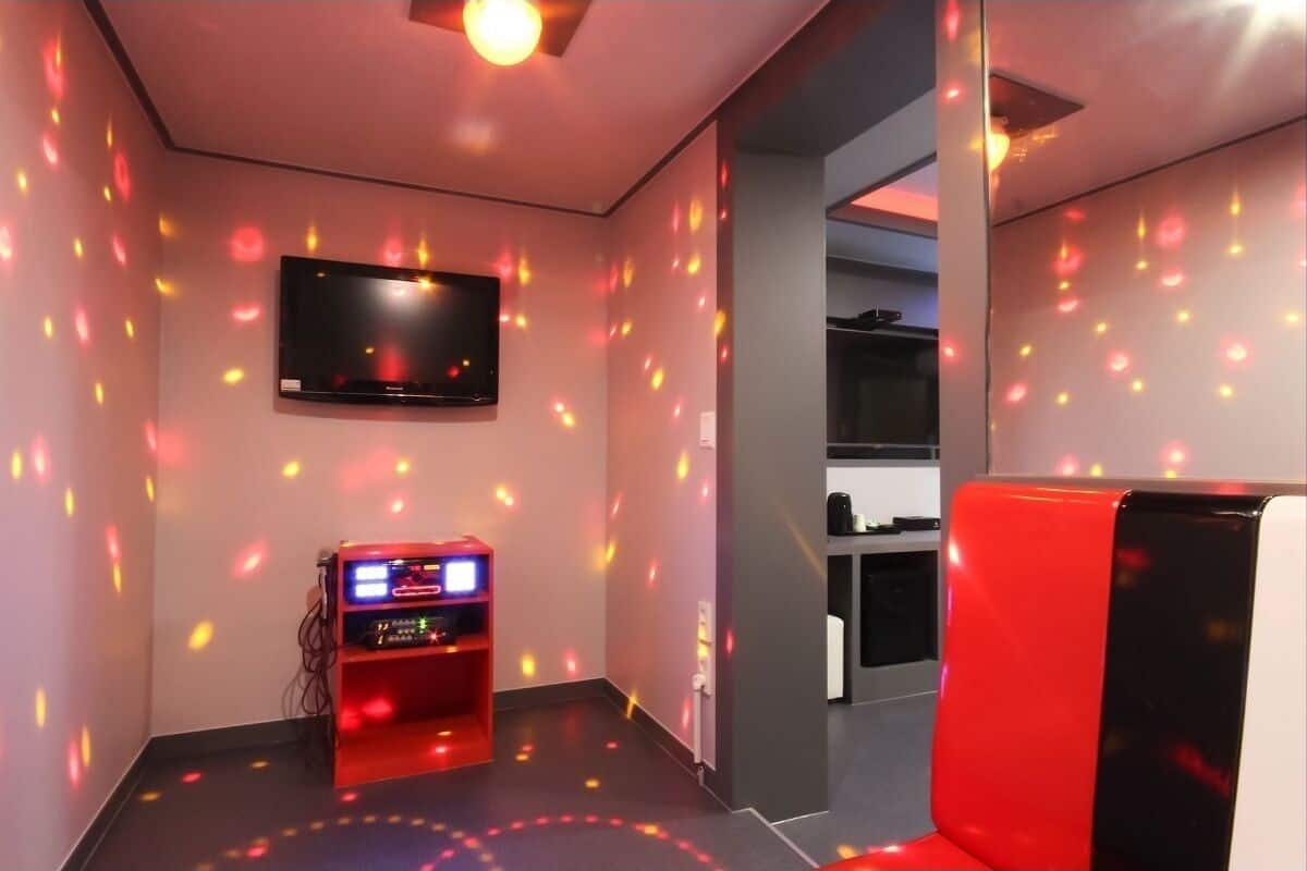 A room with a flat-screen TV mounted on the wall, a red gaming machine, and a red chair.