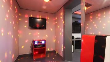 A room with a flat-screen TV mounted on the wall, a red gaming machine, and a red chair.
