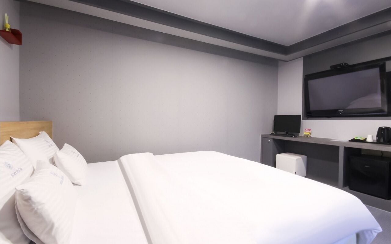 A hotel room with a bed, a desk, a television, and a coffee machine.