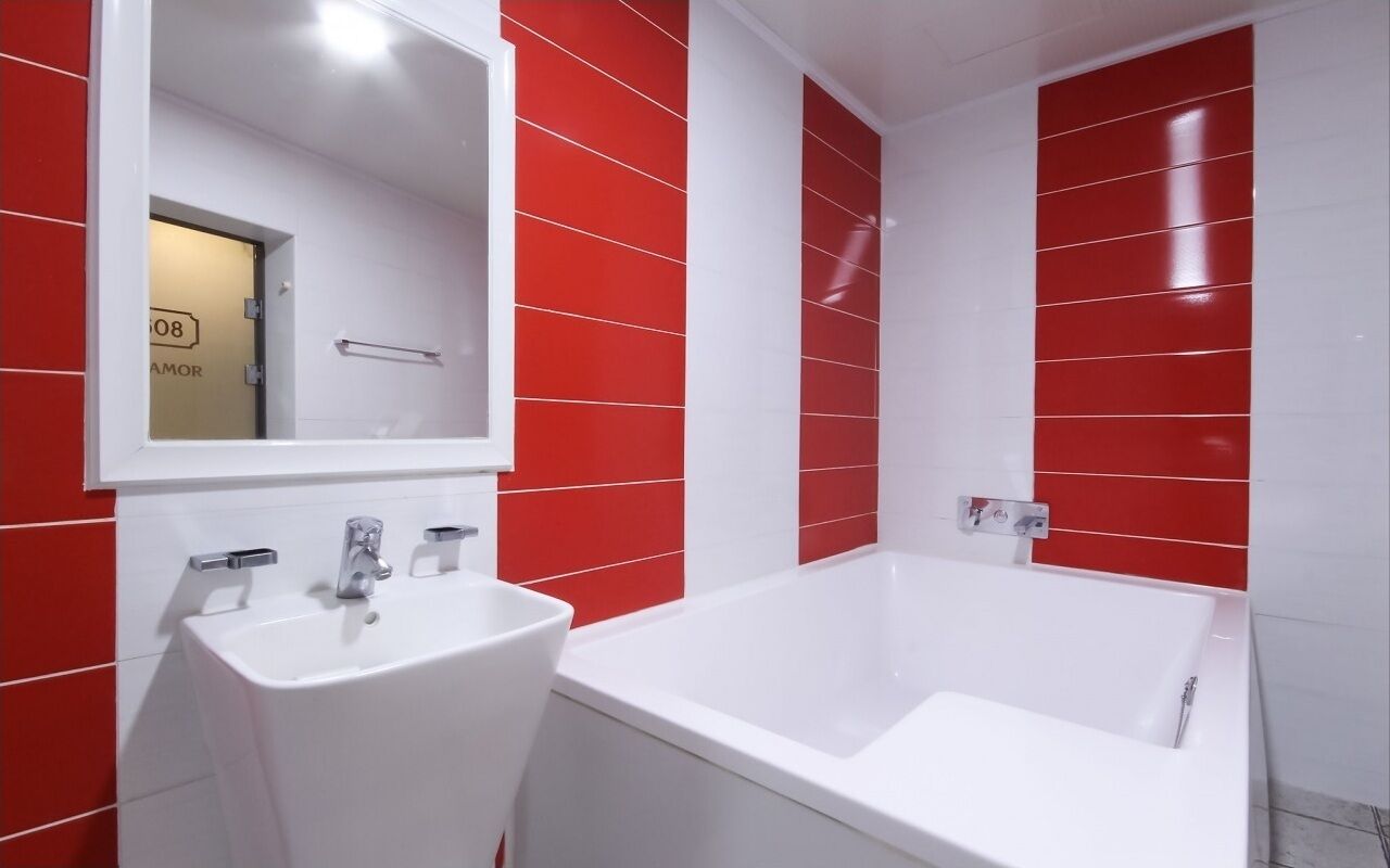 A modern bathroom with a white sink and bathtub, red and white tiled walls, and a mirror above the sink.