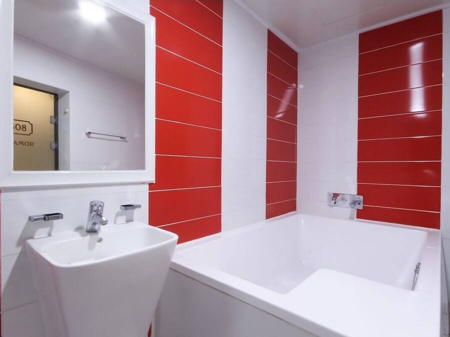 A modern bathroom with a white sink and bathtub, red and white tiled walls, and a mirror above the sink.