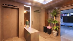 An elevator area with a reception desk, potted plants, and a clear view of the elevator doors. - AmorHotelgimhae (Gimhae)