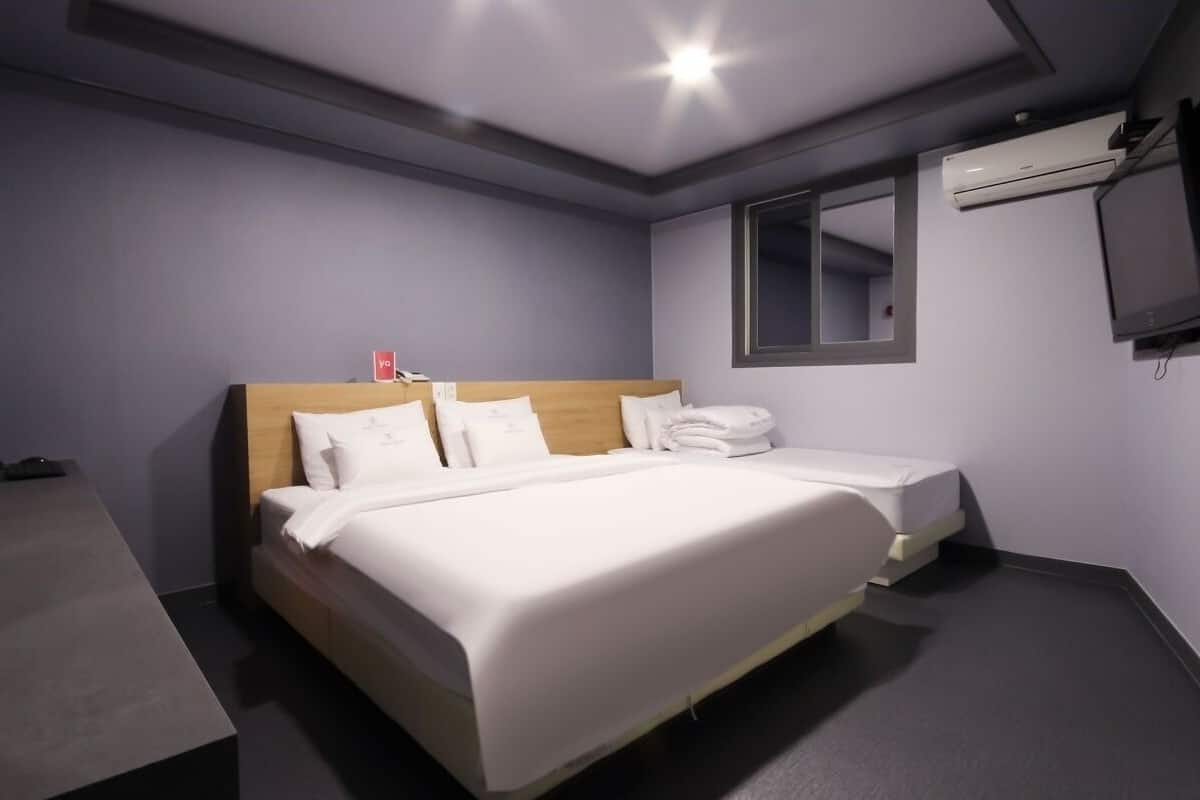 A hotel room with a large bed, a bedside table, a flat-screen TV, and an air conditioning unit.