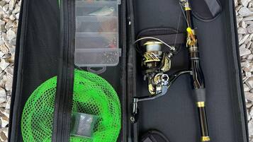 Una caja de pesca abierta con un bolsillo de malla verde, una caña de pescar y un carrete de hilo de pescar.