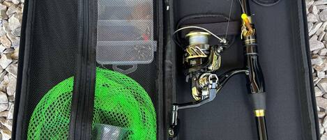 An open fishing tackle box with a green mesh pocket, a fishing rod, and a spool of fishing line.