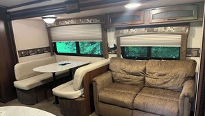 Un intérieur de camping-car compact comprenant un coin repas, un canapé et une fenêtre donnant sur un paysage verdoyant.