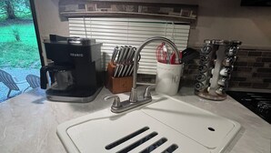 Une cuisine avec un évier blanc, une machine à café Keurig et un porte-ustensiles.