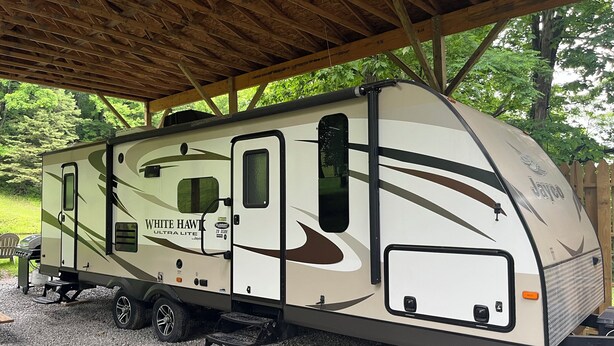 Un véhicule récréatif White Hawk ULTRA LITE est garé sous un abri en bois.