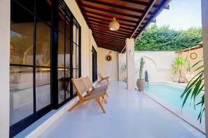 A poolside area with wooden chairs, a hanging light fixture, and potted plants. - Villa Terracotta by Pertama Stay (Canggu)