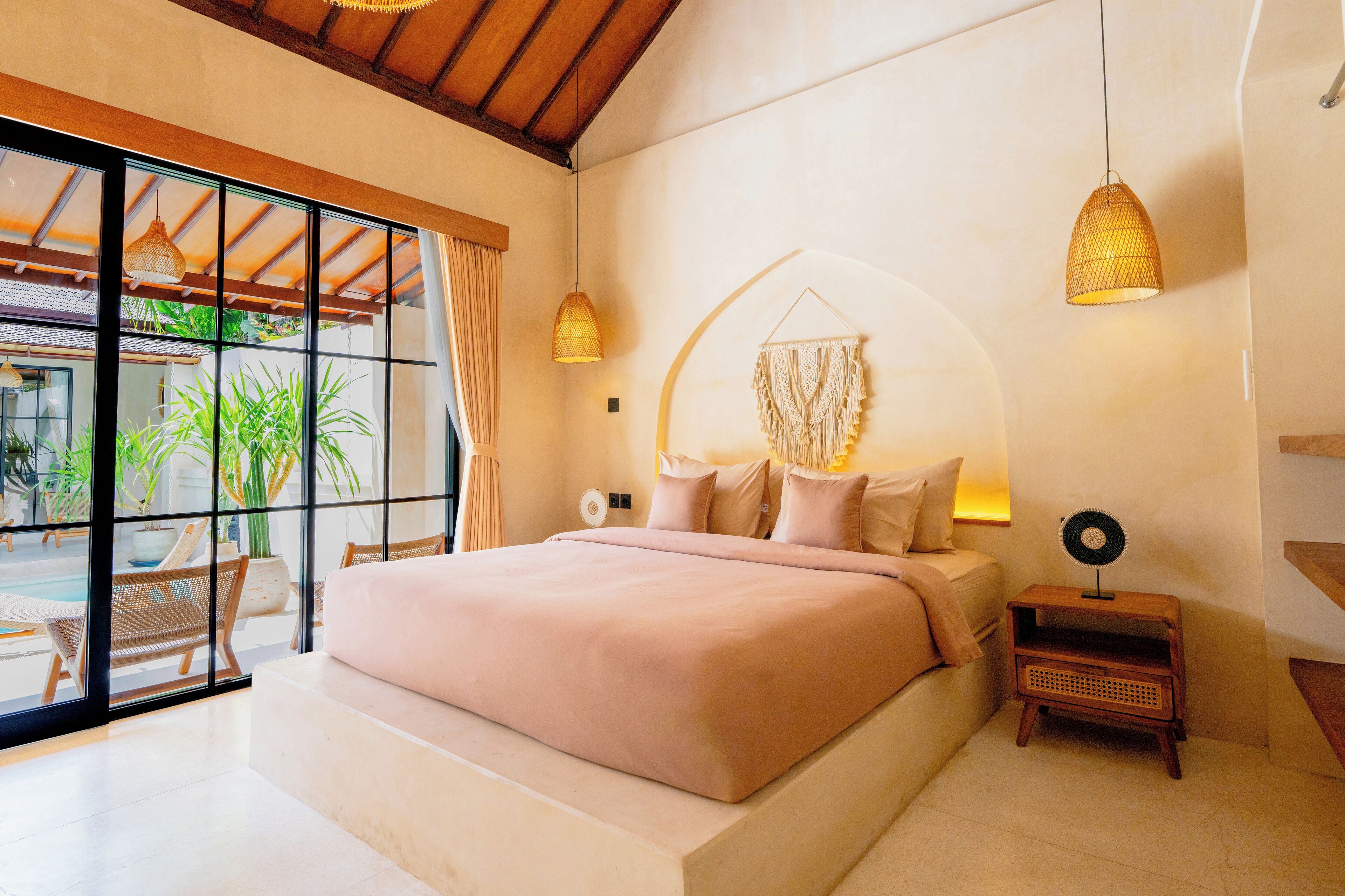 A spacious bedroom with a large bed, a view of the outdoors, and a small bedside table with a lamp.