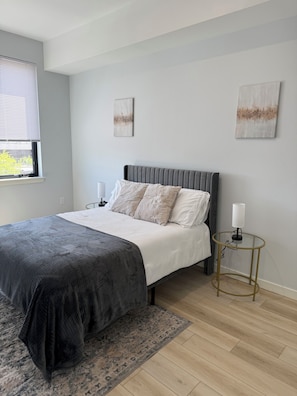 Une chambre à coucher avec un lit, des tables de chevet, une fenêtre et des œuvres d’art accrochées aux murs.
