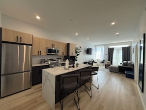 A modern kitchen with stainless steel appliances, a central island with bar stools, and a dining area with a TV.