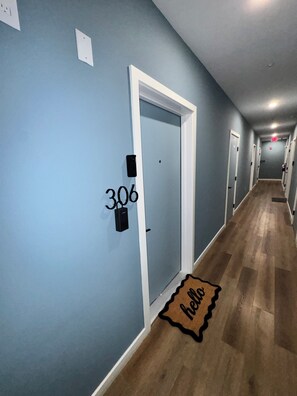 A hallway with a blue wall, a door labeled '306', a 'hello' mat, and a wooden floor.