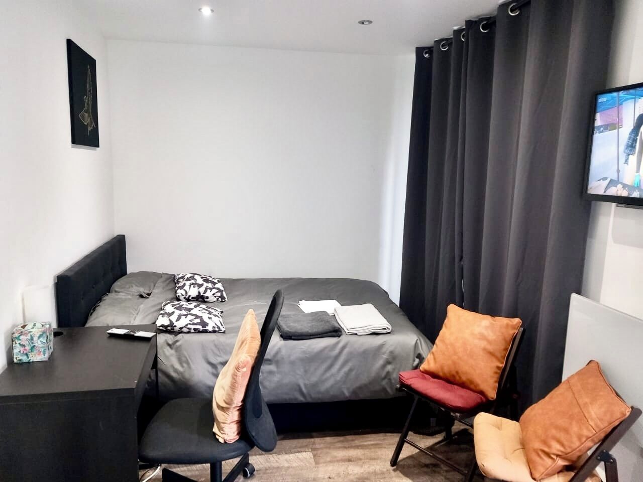 A modern hotel room with a bed, a desk, a chair, and a TV.