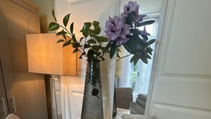 Una habitación con un amplio ventanal, un florero con flores y una lámpara.