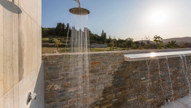 A modern outdoor shower with a stone wall backdrop and a clear sky.