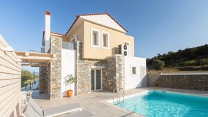 A modern villa with a stone facade, a swimming pool, and outdoor seating.