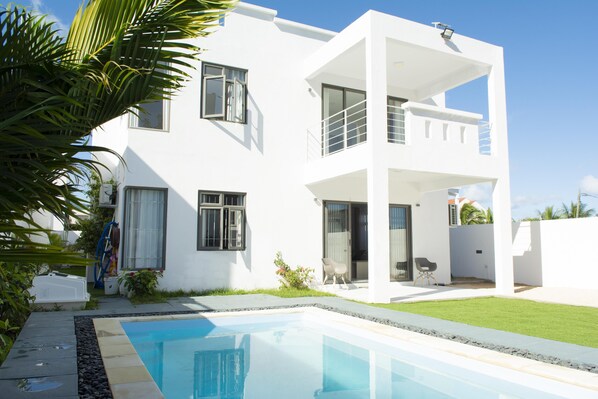 Una casa moderna de dos pisos con piscina, ventanas amplias y un balcón.