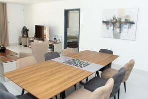 Una habitación de hotel moderna con una mesa de comedor de madera, asientos cómodos, un televisor, una cama y una pintura de un paisaje urbano.