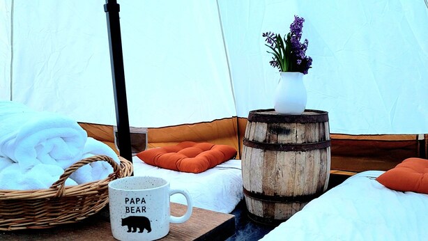 A tented accommodation with a bed, a wooden table with a mug, a basket, and a vase with flowers. - Secluded Mountaintop Retreat – Rustic Luxury & Panoramic Views at Freedom Farm (New Milford)