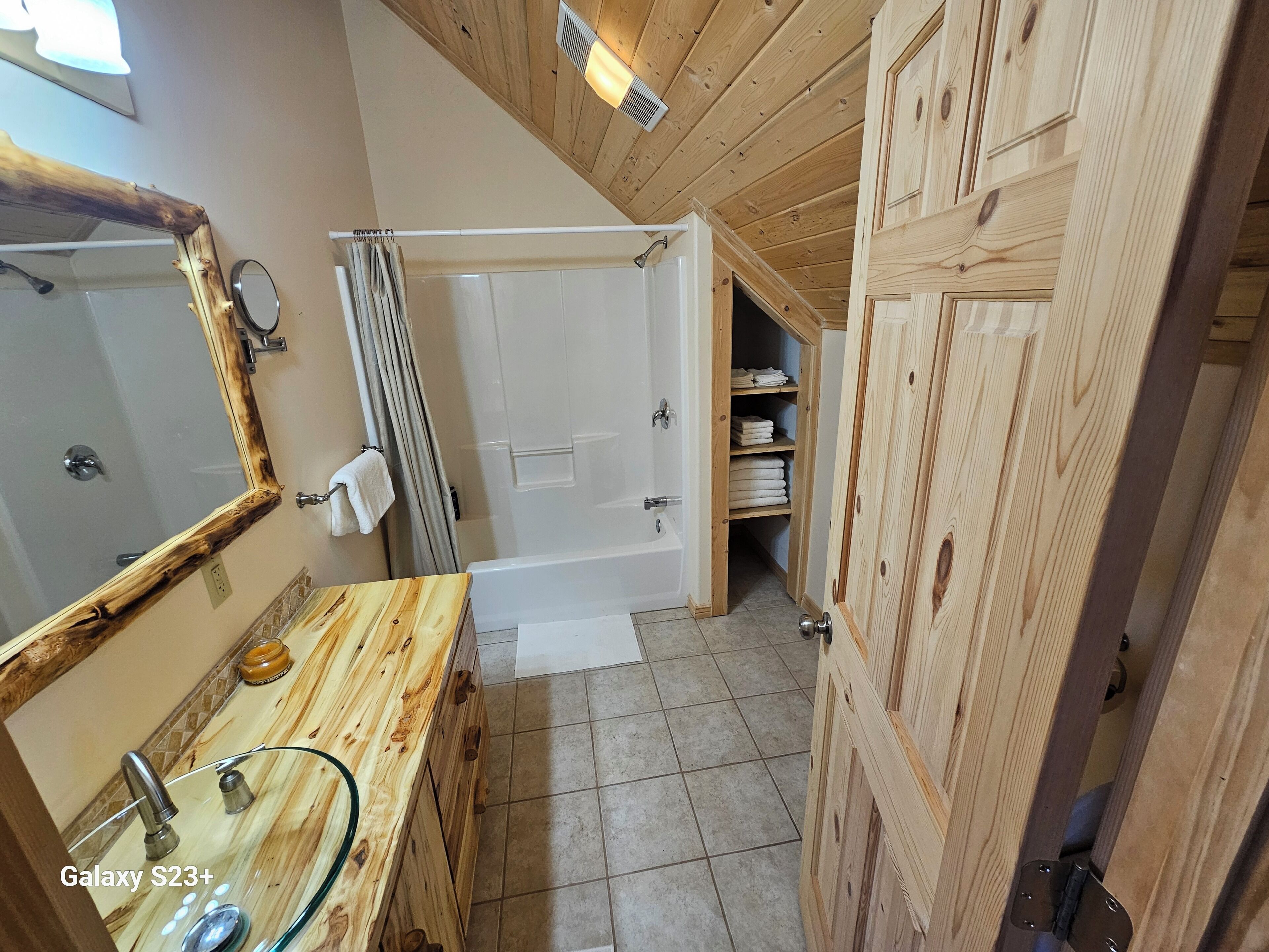Une salle de bain avec un meuble-lavabo en bois, un lavabo en verre, une baignoire et une douche.