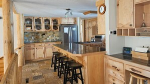 A kitchen with wooden cabinets, a central island with stools, a refrigerator, a stove, and a clock. - Gilbert Creek Lodge, your Home Sweet Home in the Uinta's! (Mountain View)