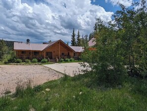 A wooden lodge with a metal roof, surrounded by greenery and a gravel driveway. - Gilbert Creek Lodge, your Home Sweet Home in the Uinta's! (Mountain View)