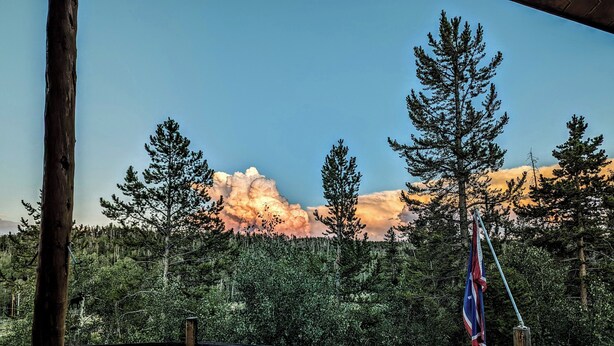 A wooden deck with a picnic table, surrounded by a wooden fence, overlooking a forested area with a flagpole. - Gilbert Creek Lodge, your Home Sweet Home in the Uinta's! (Mountain View)