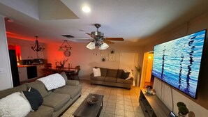 A living room with a sofa, coffee table, and TV. There is a dining area with a table and chairs.