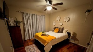 A bedroom with a bed, a ceiling fan, a nightstand, a lamp, a rug, and a wooden floor.
