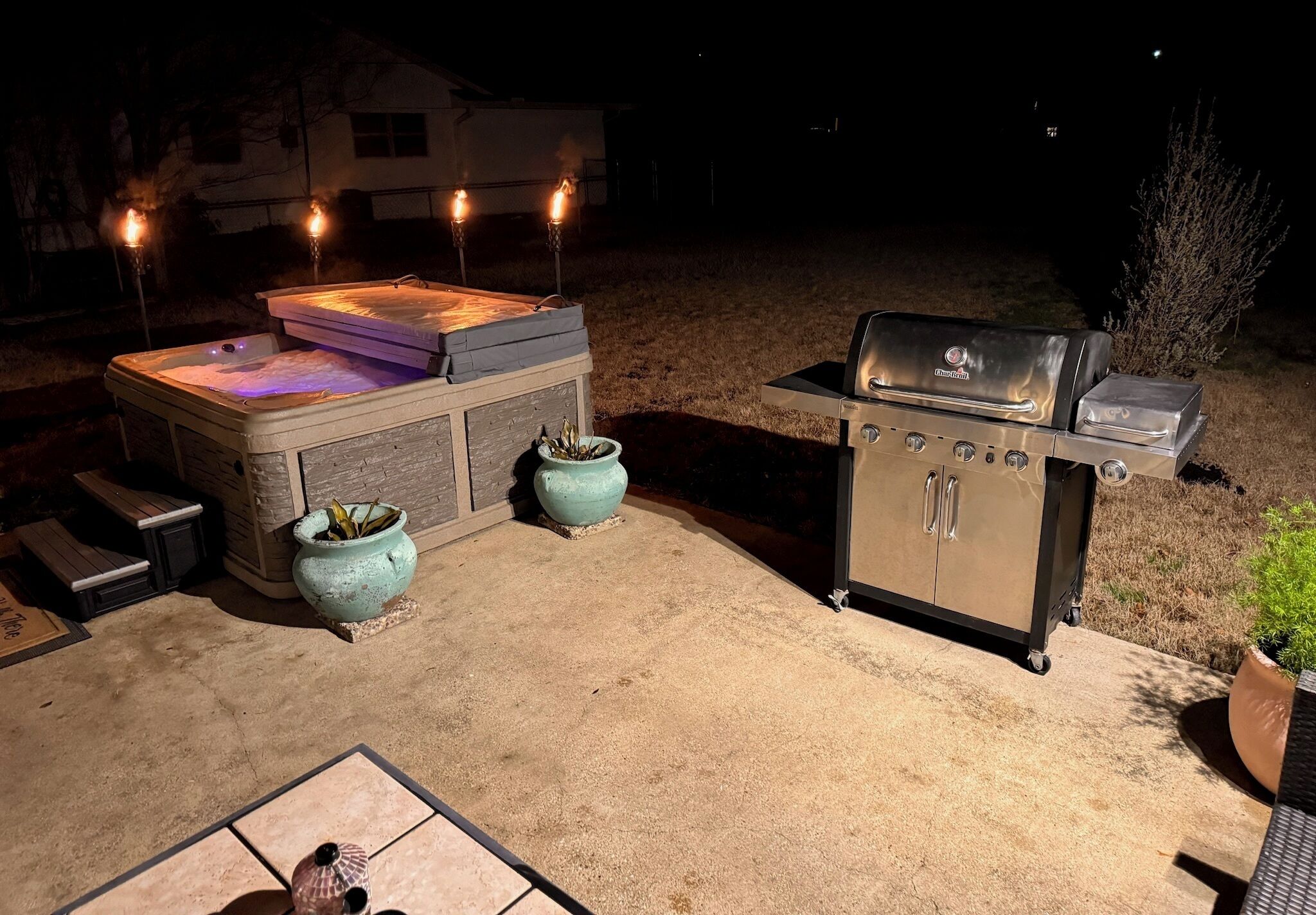 An outdoor patio with a hot tub, a grill, and two large planters.