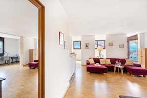 Ampla sala de estar com sofá vermelho, mesinha de centro e vista da cidade através de grandes janelas.