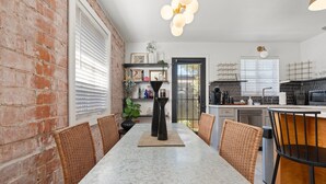 Un comedor con una mesa de mármol, sillas de mimbre y una pared de ladrillo.