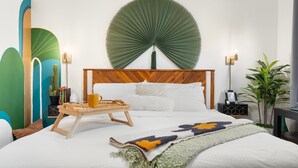 Una habitación de hotel con una cama grande, un cabecero de madera, un adorno circular en la pared, una mesita de noche con una bandeja y una planta en maceta.
