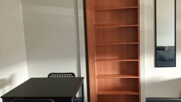 Una habitación con alfombra gris oscuro, una mesa negra con dos sillas y una estantería de madera contra la pared.