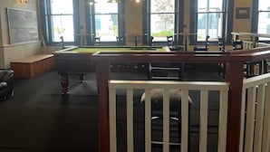 A pool table in a room with large windows, a billiards table, and a seating area with a bench. - Australia Hotel Fremantle (Fremantle)