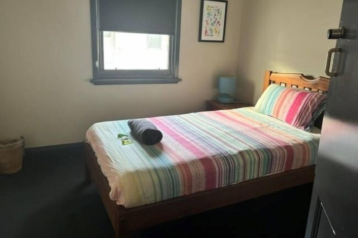 Une chambre à coucher avec un lit, une fenêtre, une table de chevet et un tableau accroché au mur.