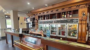 A bar area with a wooden counter, a cash register, and a refrigerated display case with various beverages. - Australia Hotel Fremantle (Fremantle)
