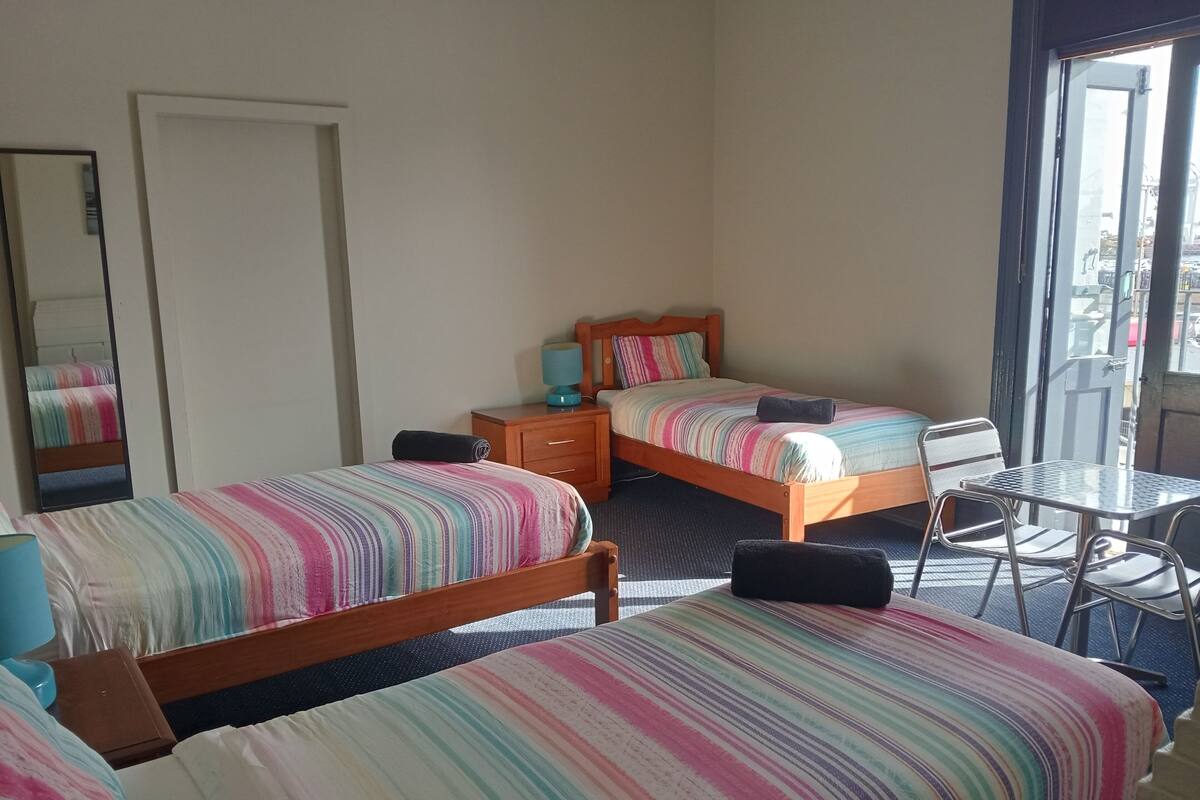Une chambre d’hôtel avec deux lits simples, une commode en bois, une petite table et une chaise.